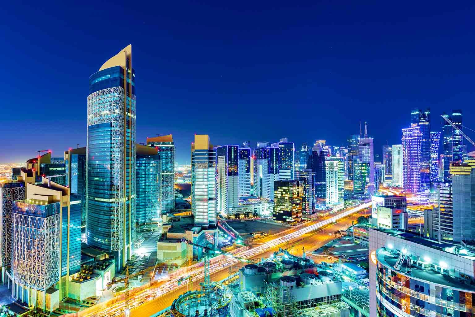 Qatar Visa Doha skyline at dusk with illuminated skyscrapers and busy city streets, Qatar urban landscape